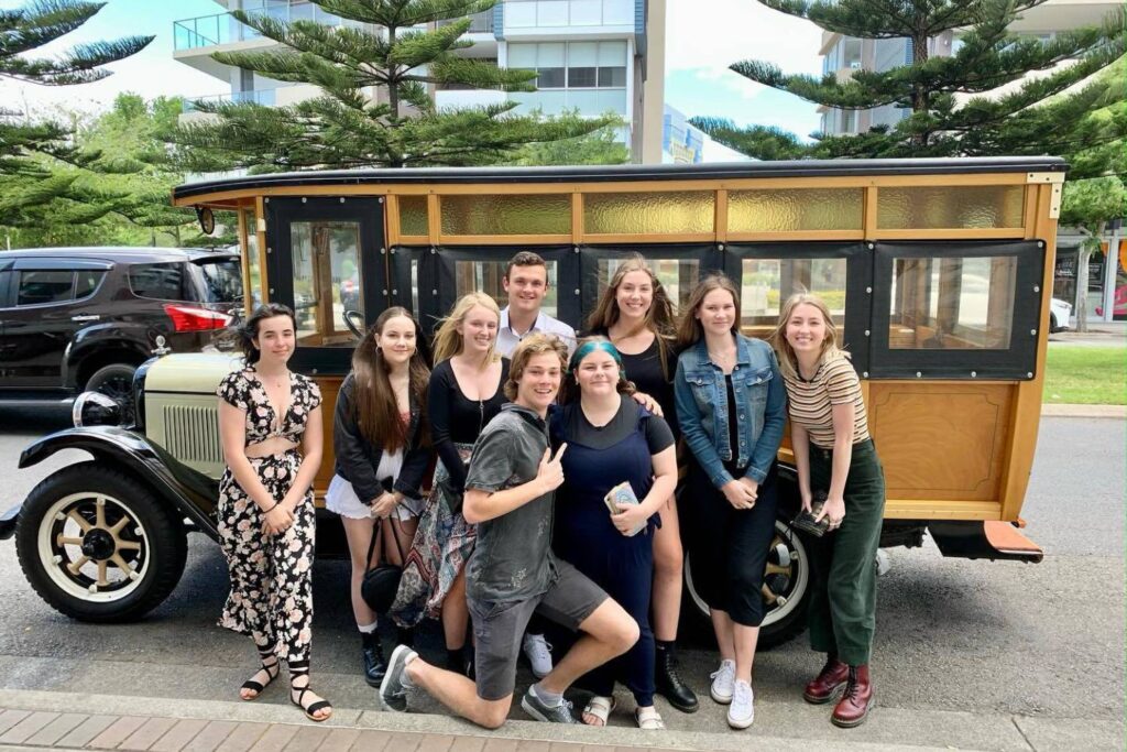 Group of young people posing in front of a vintage woody bus parked on a city street.
